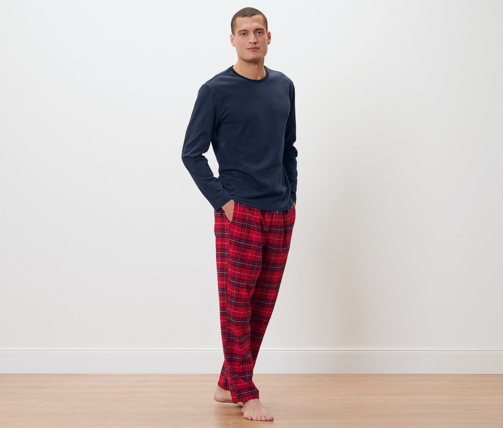 Muž pózuje v tmavě modrém pyžamovém topu a kostkovaných flanelových kalhotách.