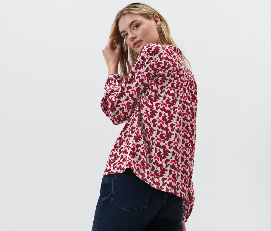 Žena se dívá přes rameno a pózuje v halence s potiskem.