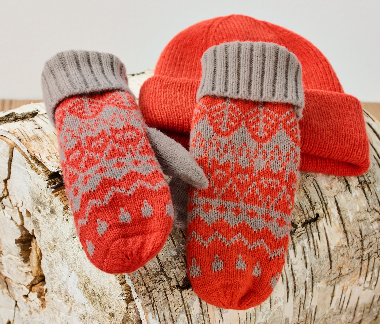 Pletené palčáky a oranžová pletená čepice leží na březovém špalku.