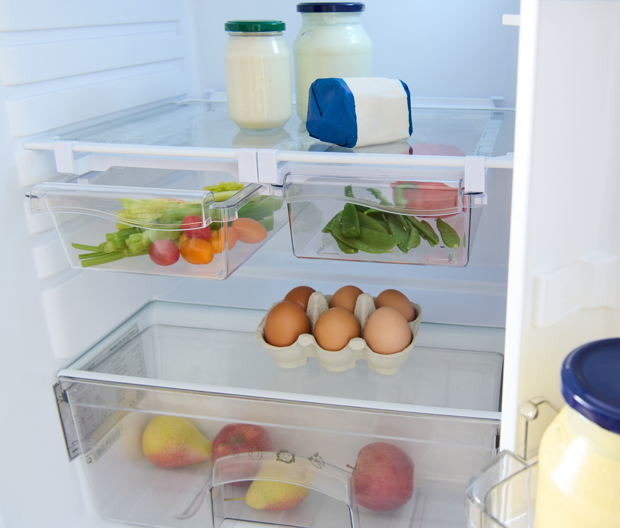 Uvnitř lednice jsou dva zásuvné boxy, sklenice, vejce a ovoce.