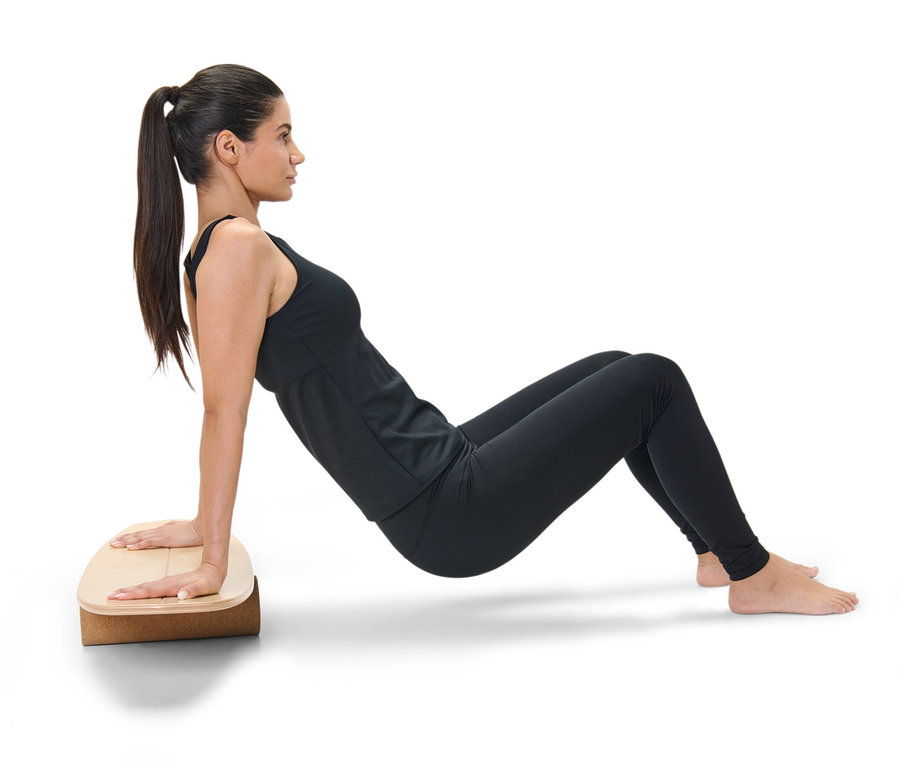 Žena v černém sportovním oblečení cvičí plank na balanční desce.