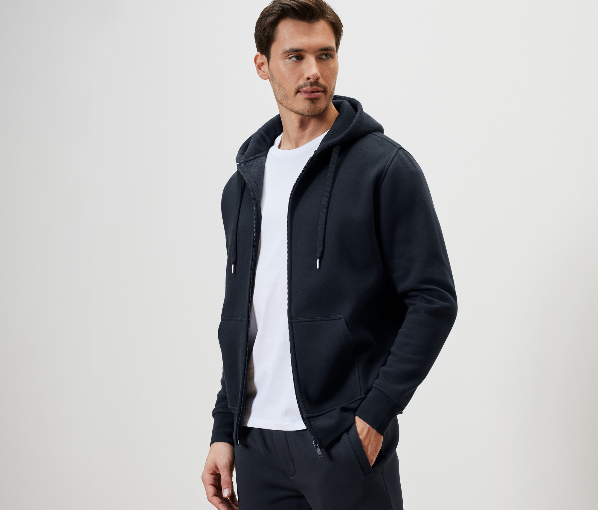 Muž má na sobě mikinu s kapucí a bílé tričko.