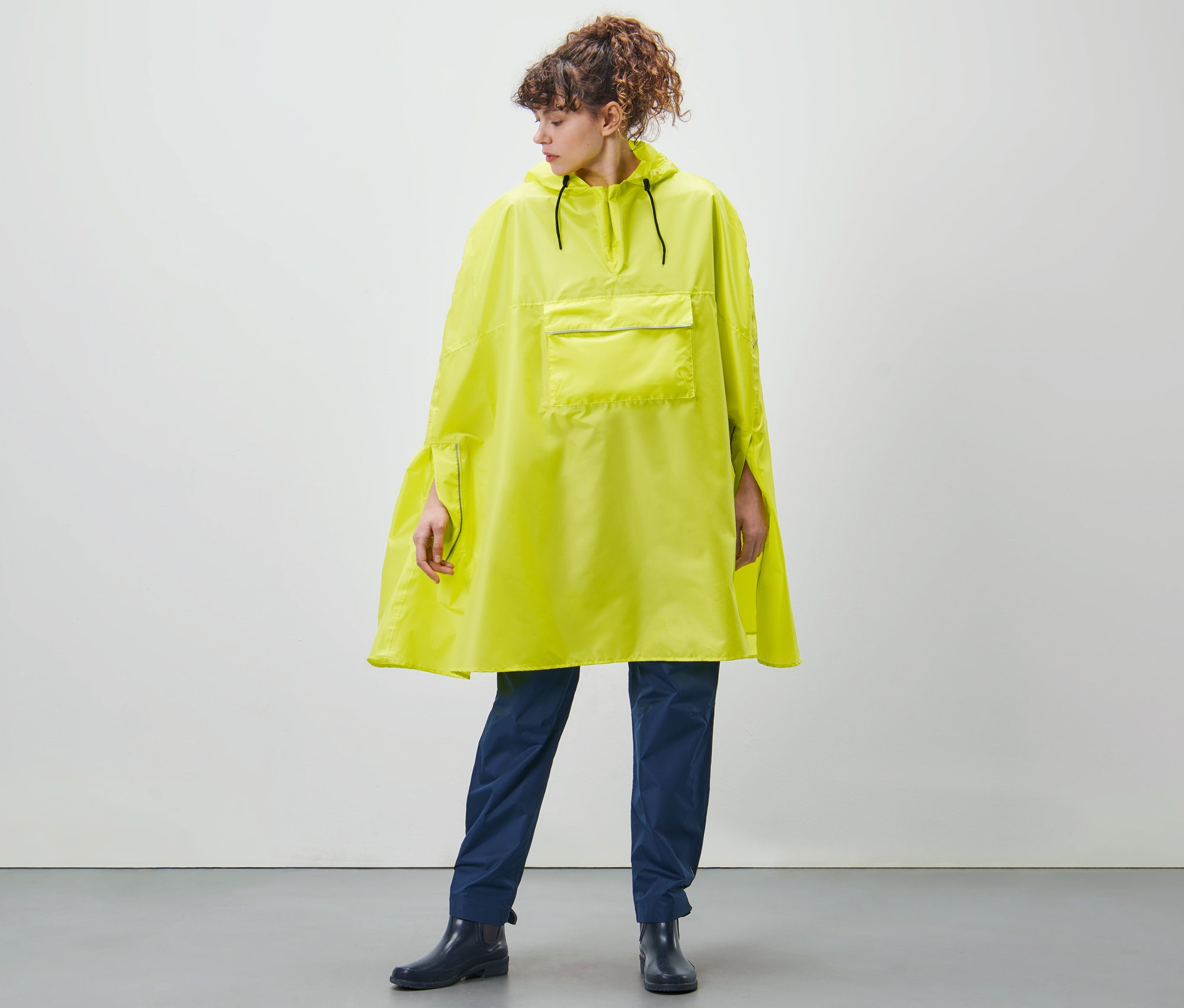 Žena stojí a má na sobě limetkové unisexové pončo do deště.