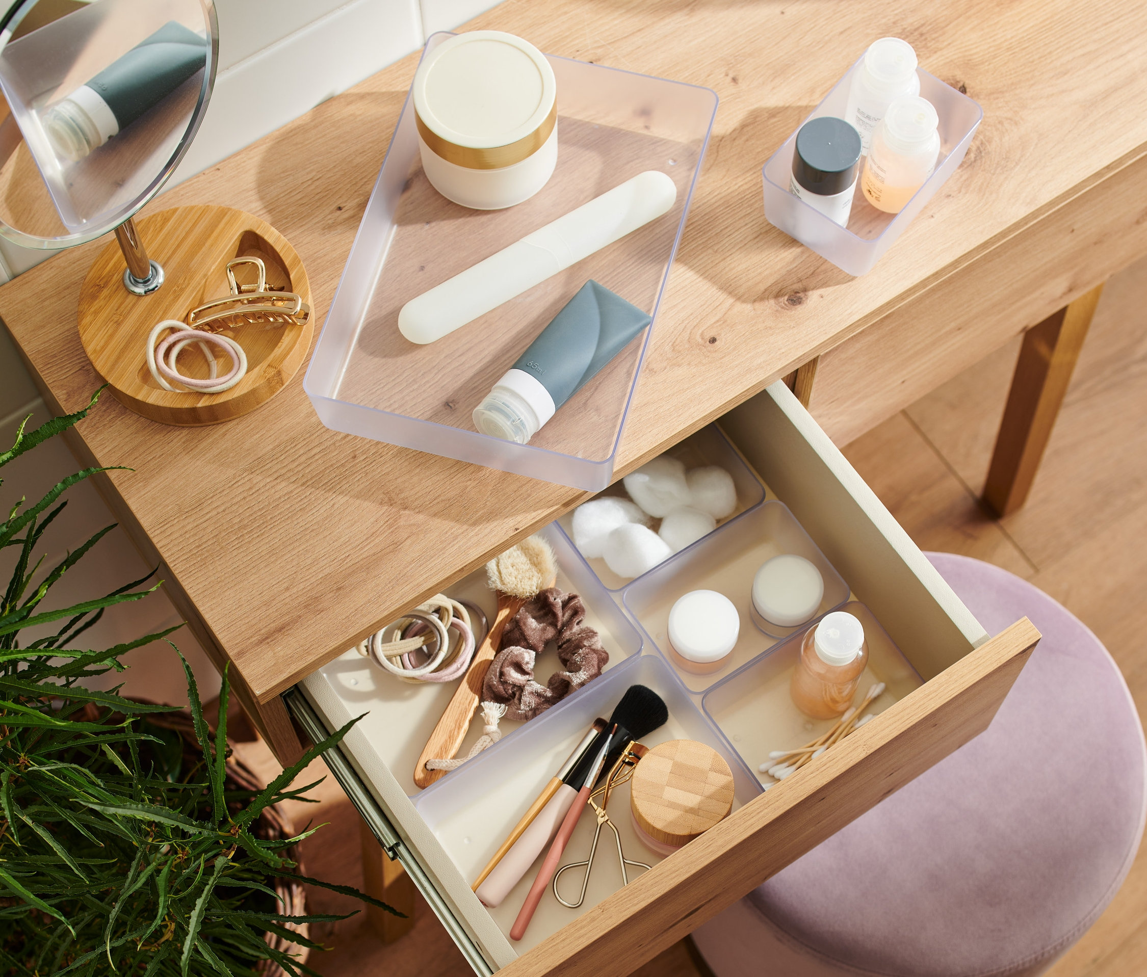 Otevřená zásuvka dřevěného toaletního stolku obsahuje sadu organizérů do zásuvky s kosmetikou.