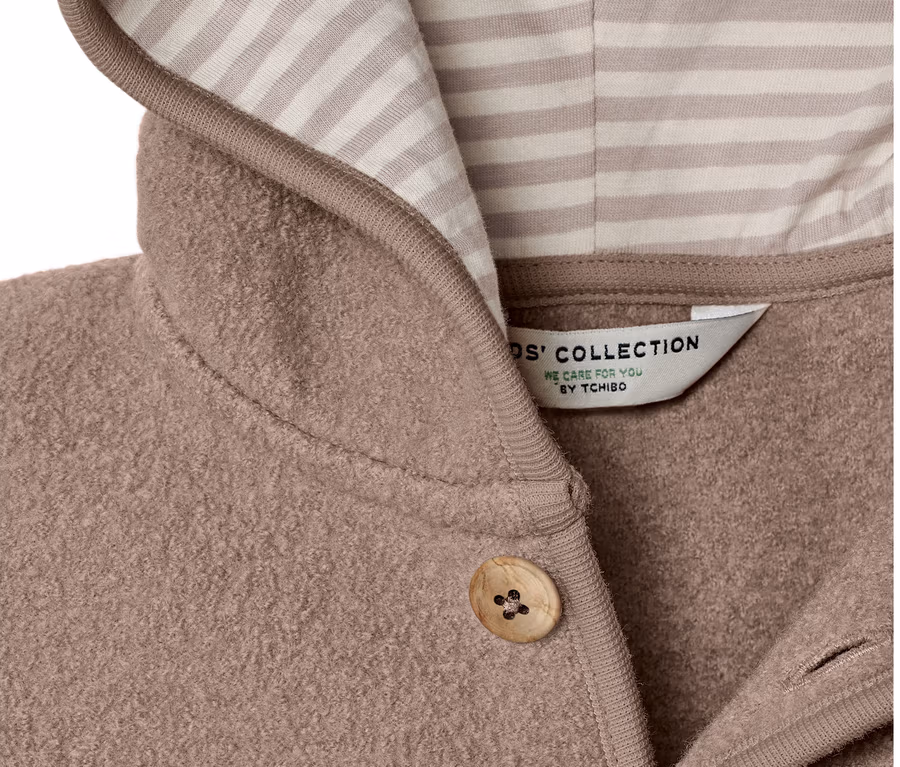 Detail dětského kabátku s vlnou merino, s kapucí s béžovými a bílými pruhy a zapínáním na knoflíky.