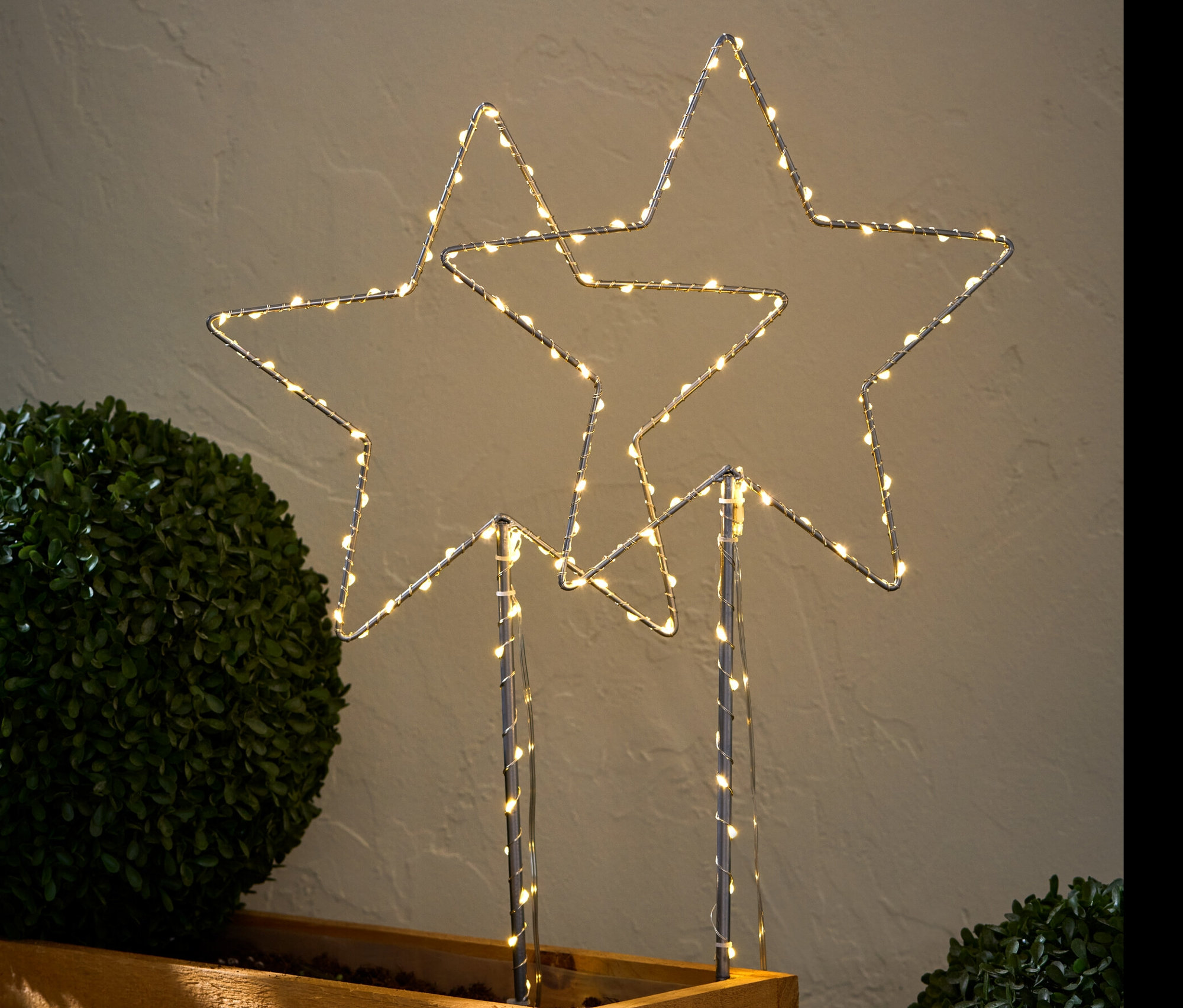 Dva velké LED bodce k zapíchnutí do země ve tvaru hvězdy umístěné v dřevěném květináči.