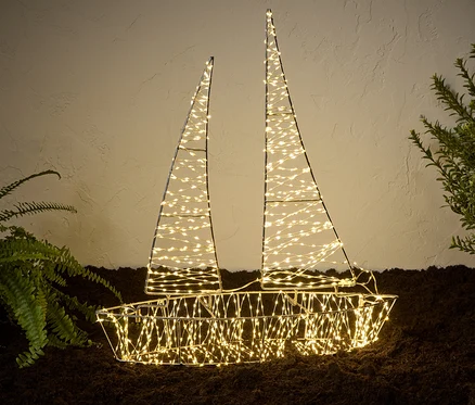 Osvětlená 3D venkovní loďka s LED dekorací stojí na zemi vedle rostlin.