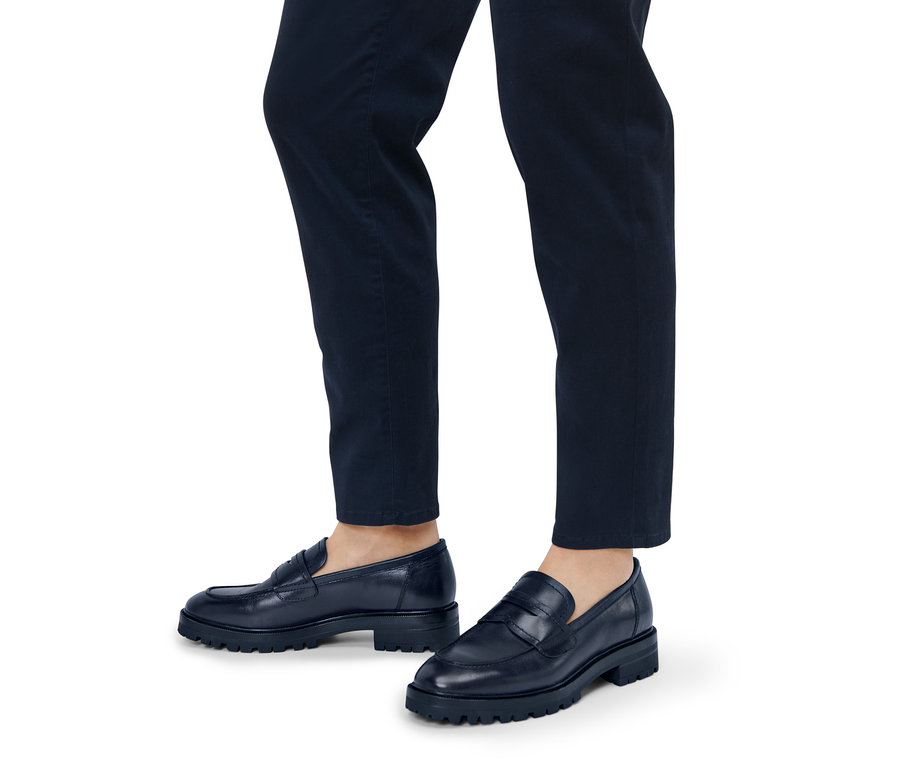 Nohy osoby v tmavě modrých kalhotách a kožených mokasínech.
