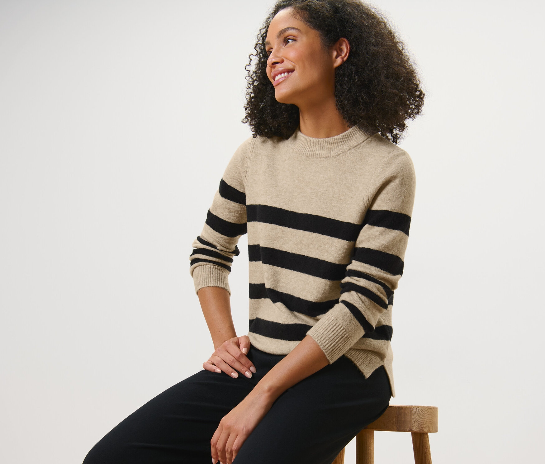 Žena sedí na stoličce a má na sobě pletený svetr s proužky.