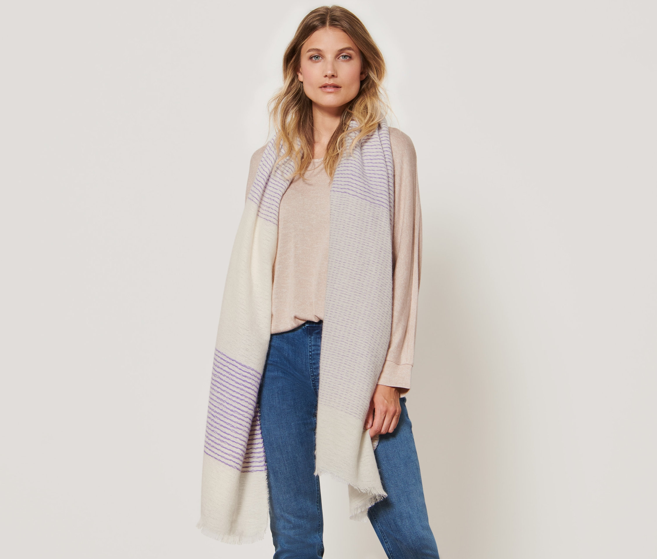 Žena pózuje s tkanou šálou s proužky.