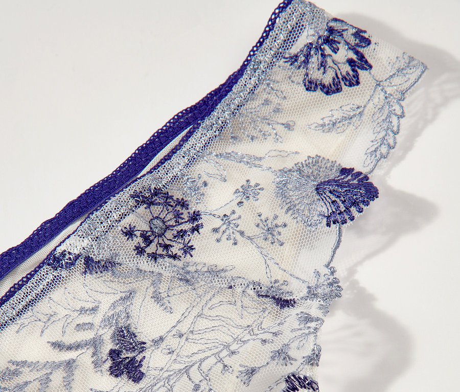 Detail bílých tang Passionata »Chloe« s modrou květinovou výšivkou.
