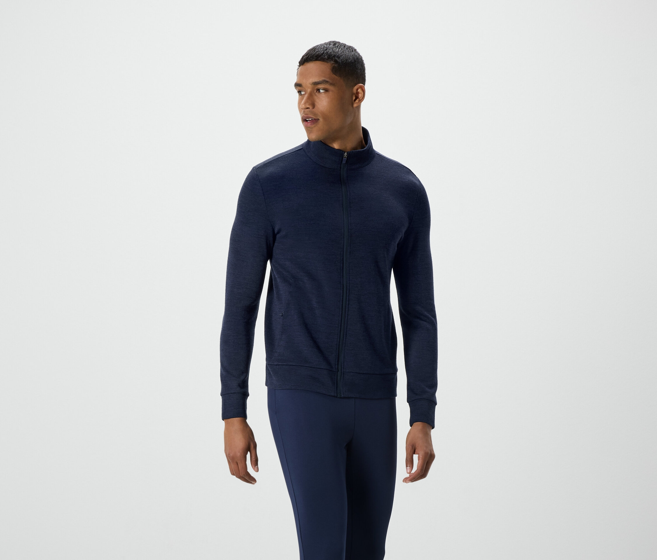 Muž v tmavě modré bundě na zip a kalhotách se dívá doleva.