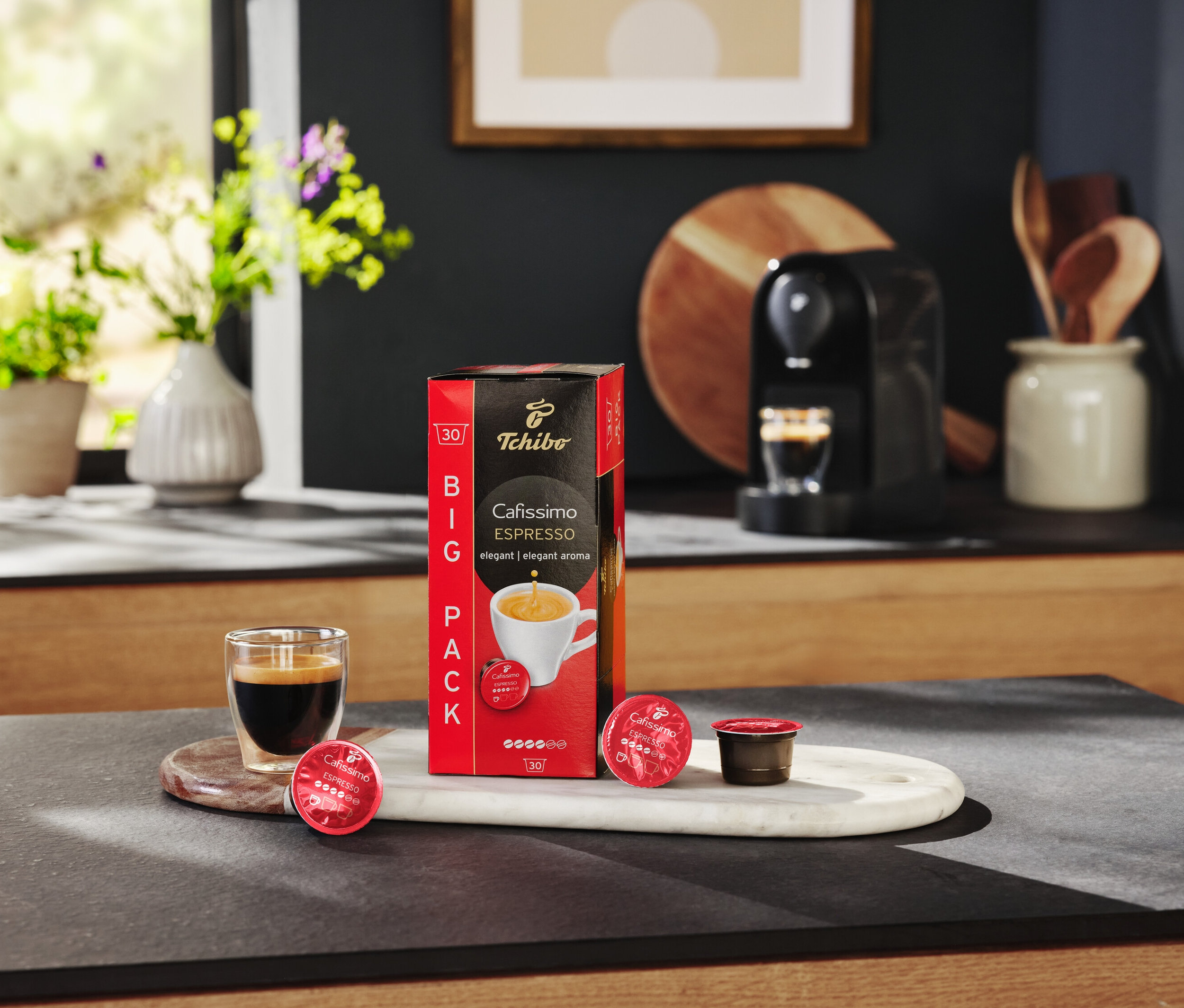 Na stole stojí balení kapslí Cafissimo Espresso, sklenice s espressem a kávovar.