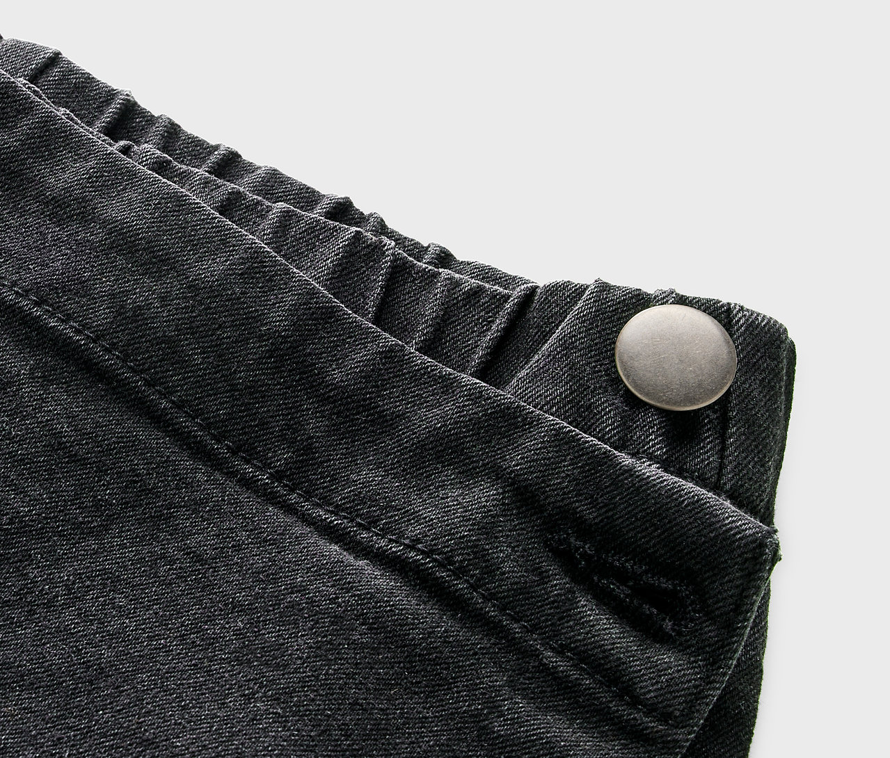 Detail dětské kalhotové sukně v džínovém vzhledu s knoflíkem.