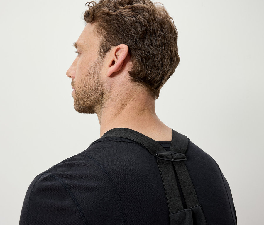 Muž s hnědými vlasy má na sobě černé tričko a černé popruhy.