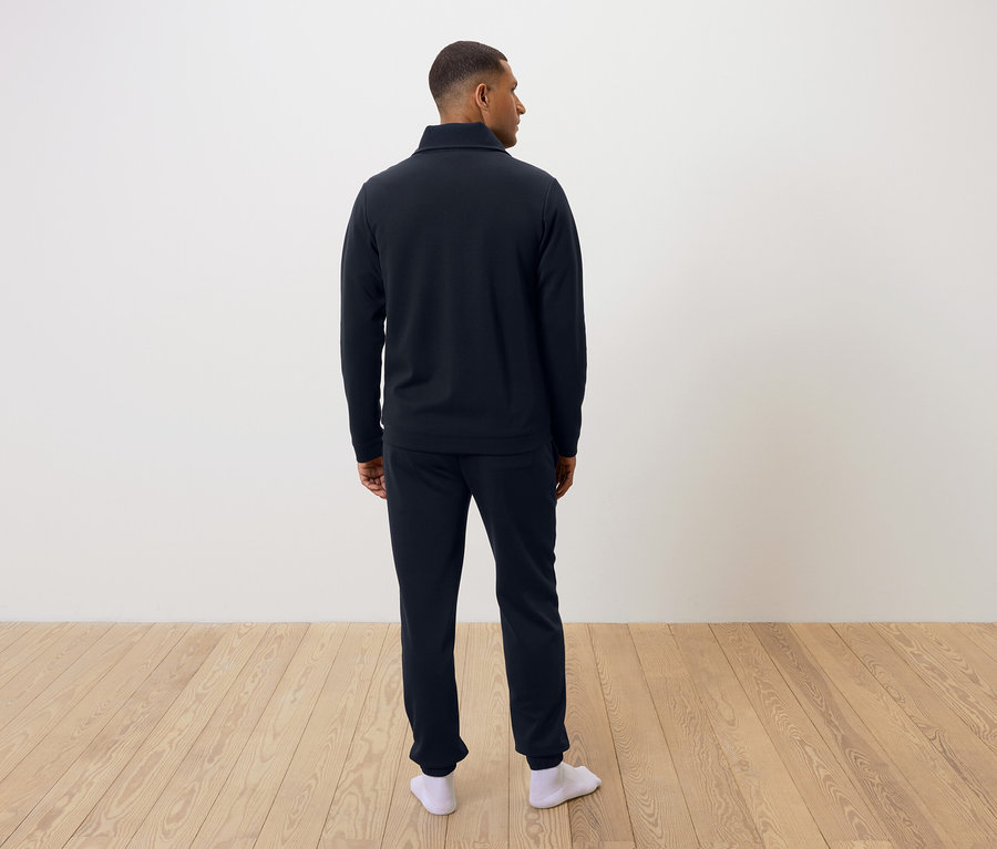 Muž zády k fotoaparátu má na sobě tmavě modré pyžamo a bílé ponožky.