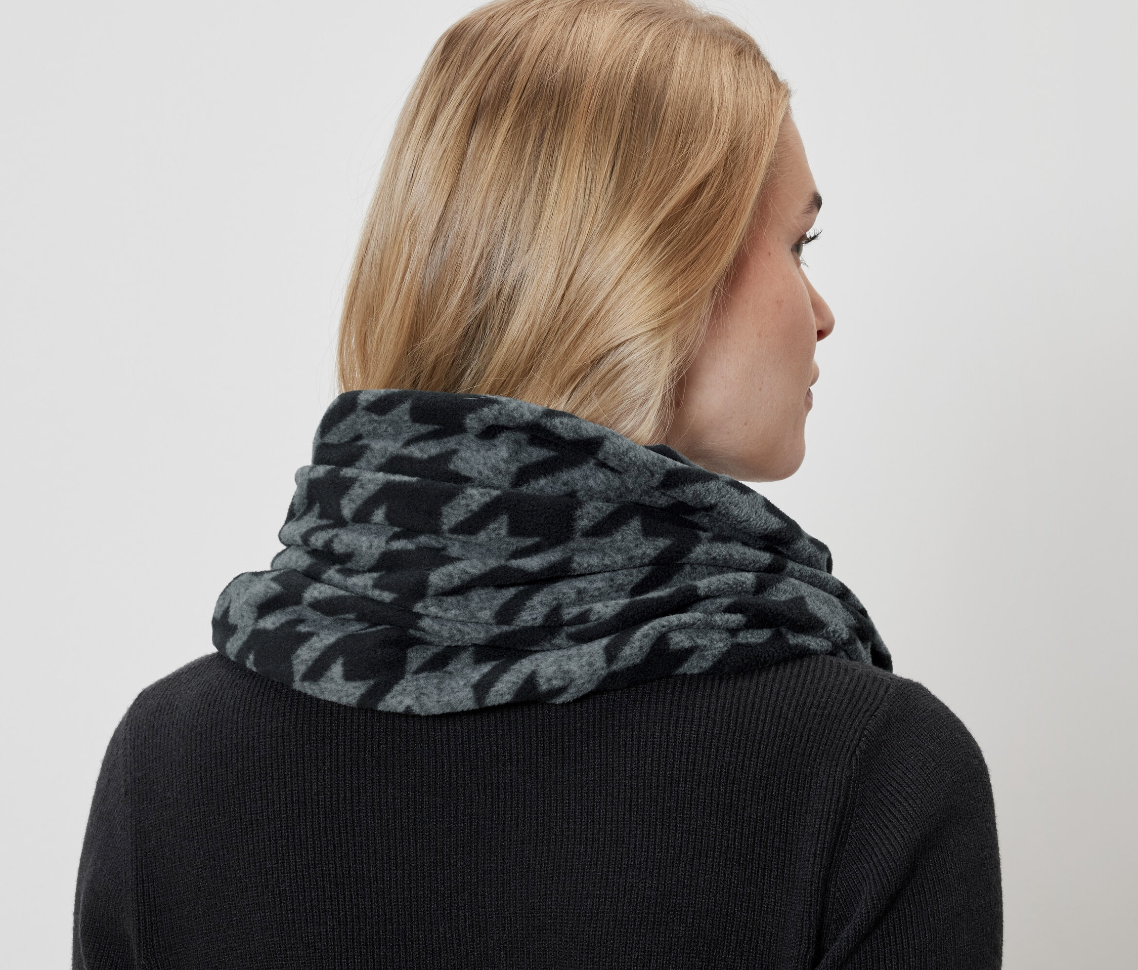 Žena má na sobě šedý a černý šátek se vzorem kohoutí stopy a černý svetr.