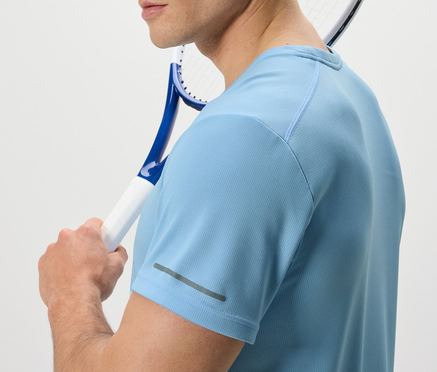 Muž s tenisovou raketou přes rameno má na sobě světle modré funkční triko.