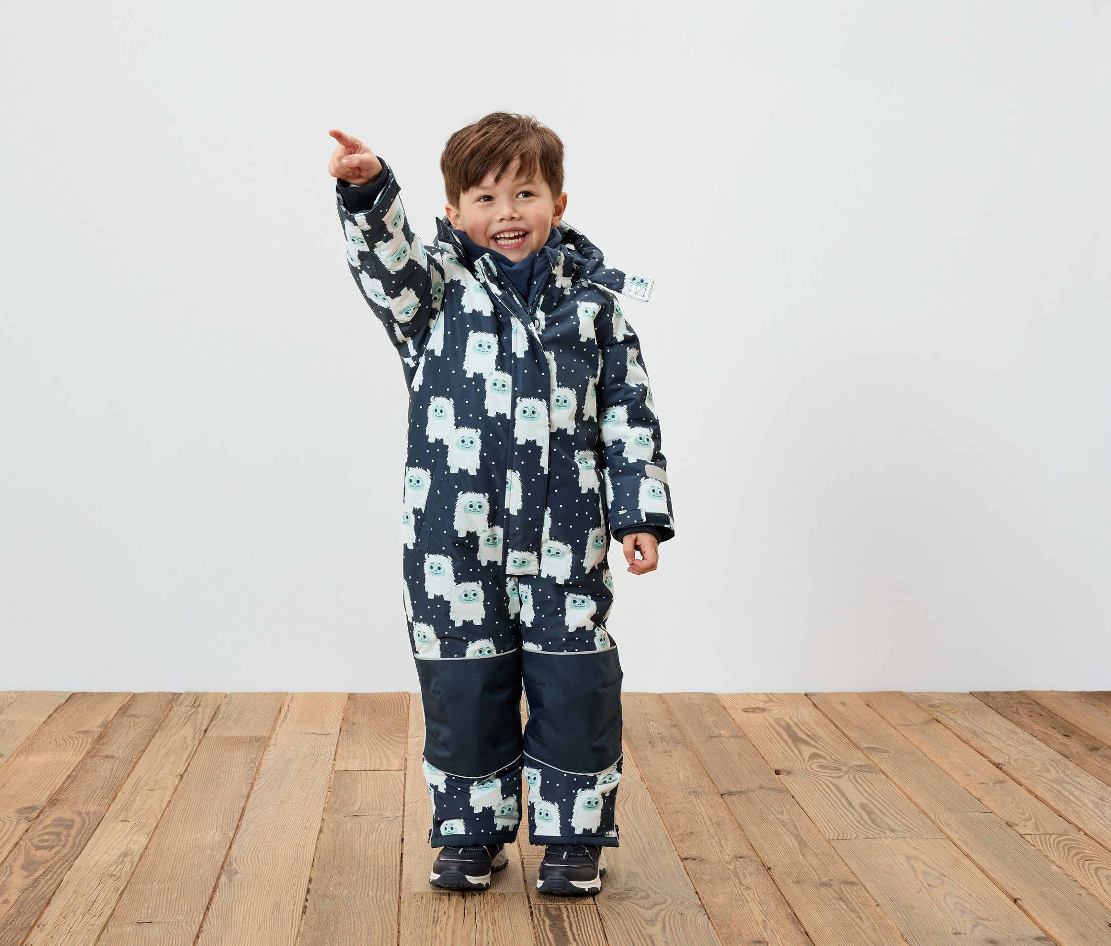Chlapec v zimní kombinéze s potiskem postaviček ukazuje prstem.