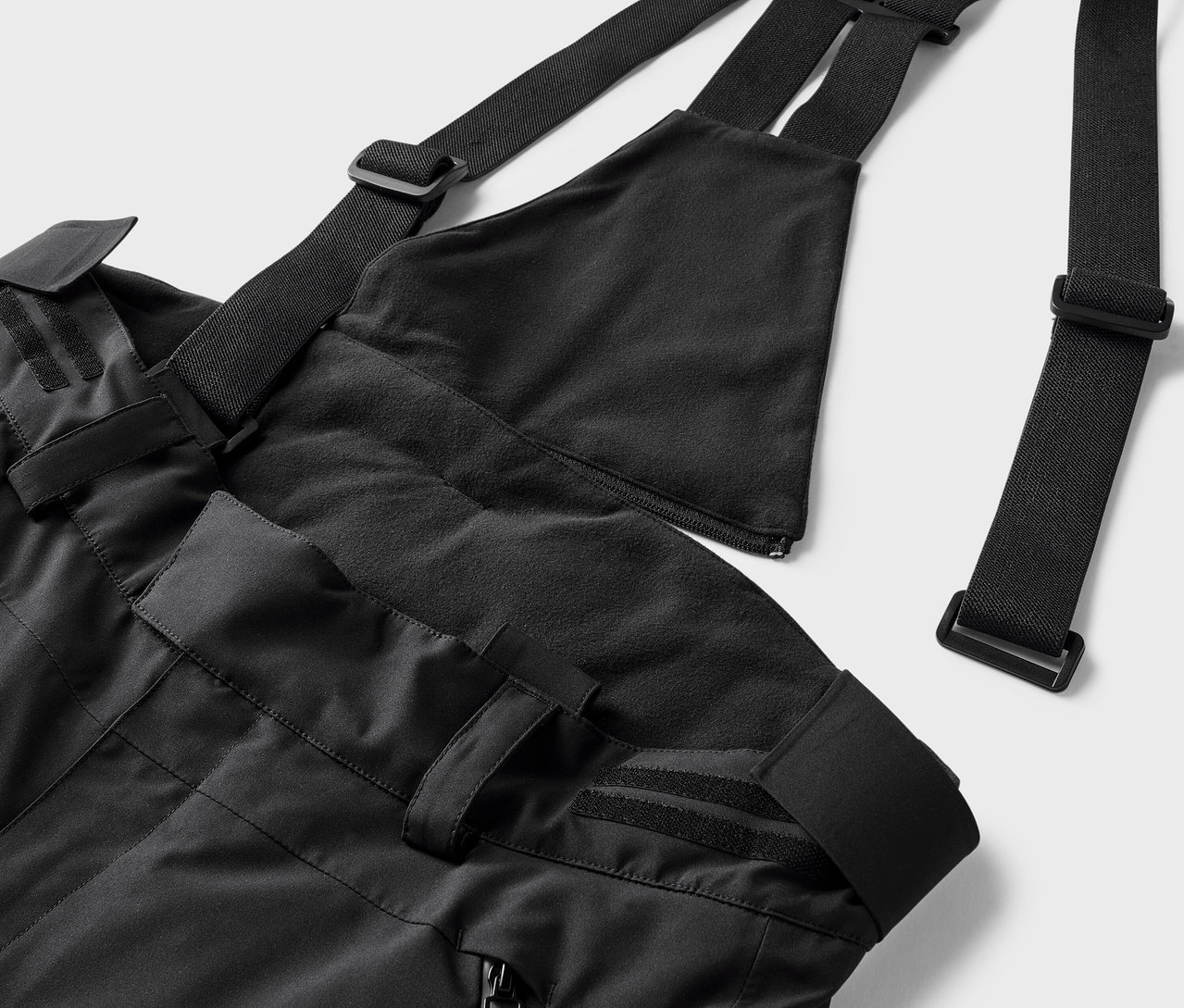 Černé lyžařské kalhoty s laclem a nastavitelnými popruhy.