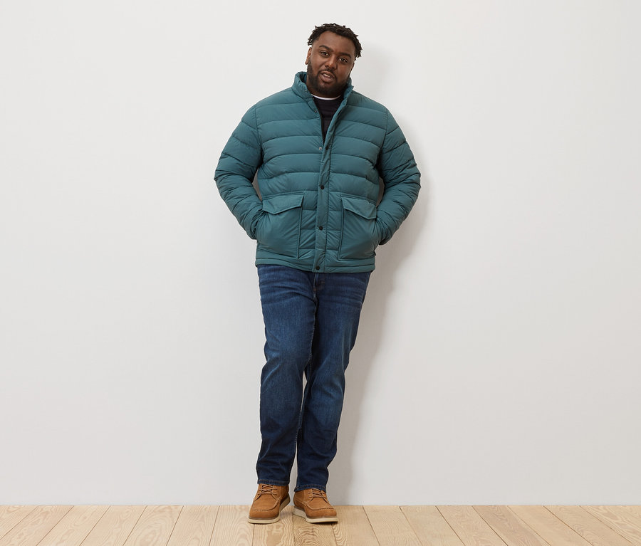 Muž stojí a má na sobě prošívanou bundu, džíny a boty.
