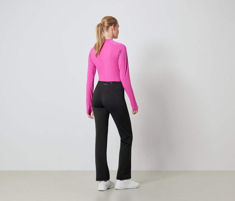 Žena zády k fotoaparátu má na sobě růžový top s dlouhým rukávem a černé kalhoty.