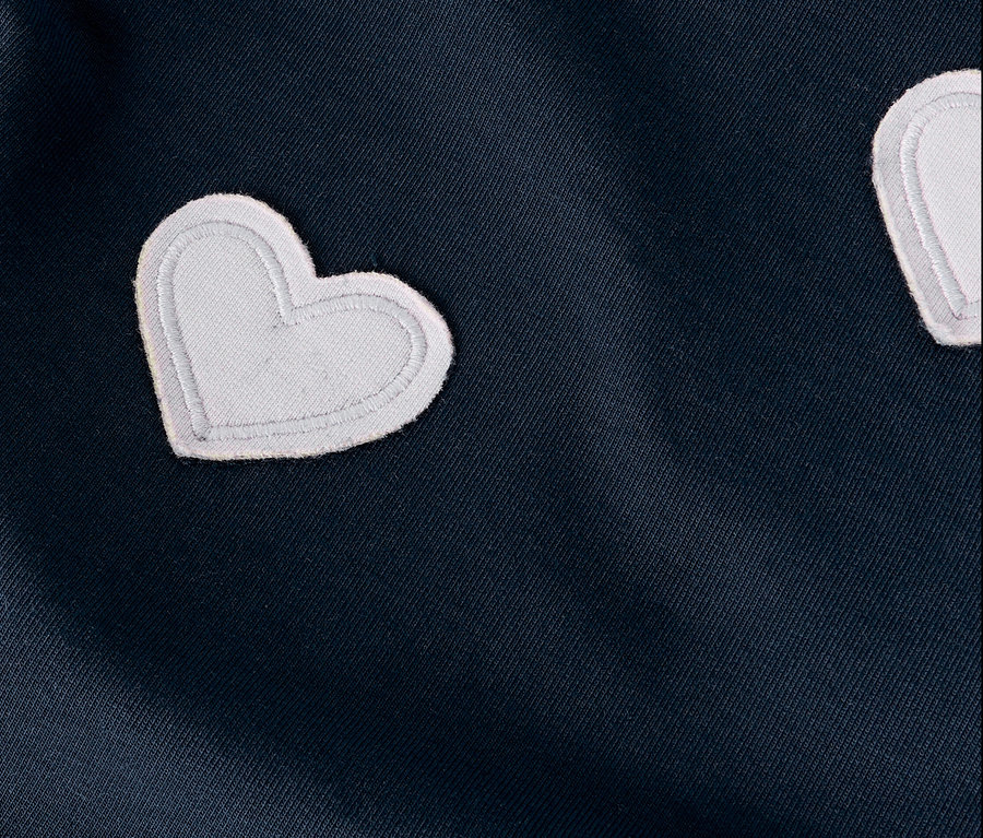 Detailní záběr tmavě modré látky s bílými aplikacemi ve tvaru srdce.