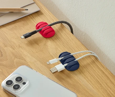 Kabel USB-C v červeném držáku kabelů, dva kabely USB v modrém držáku kabelů a smartphone na stole.