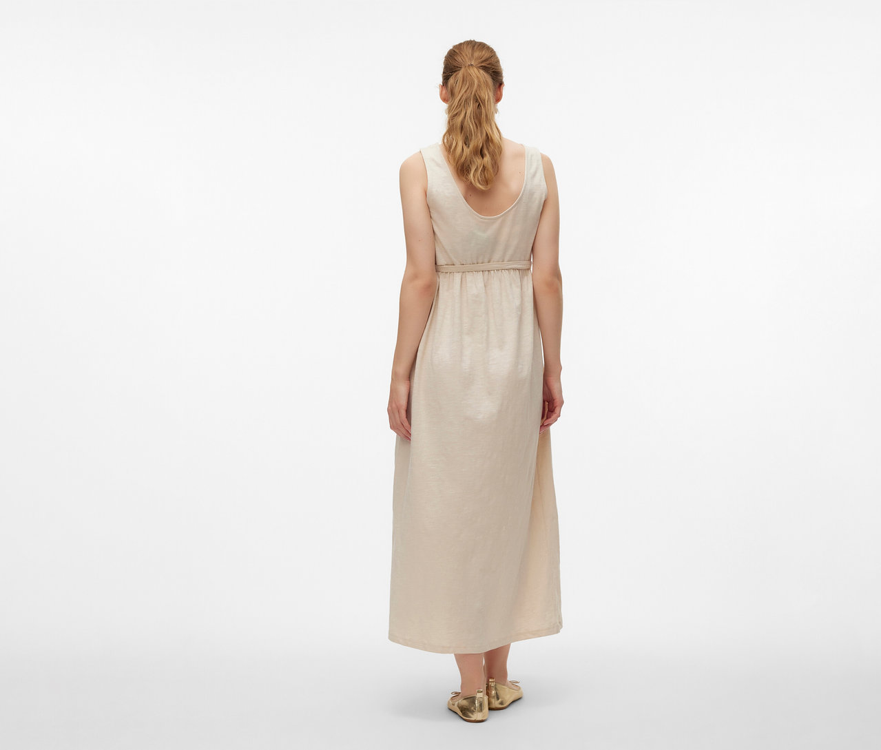 Pohled zezadu na ženu v těhotenských šatech MAMALICIOUS »MLEVI LIA« a zlatých botách na bílém pozadí.