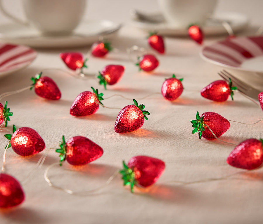 Světelný řetěz ve tvaru jahod na stole s nádobím.