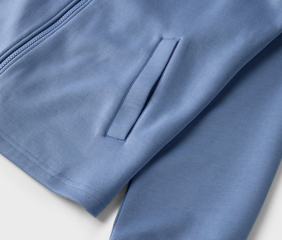 Detail světle modré sportovní bundy na zip s kapsou.