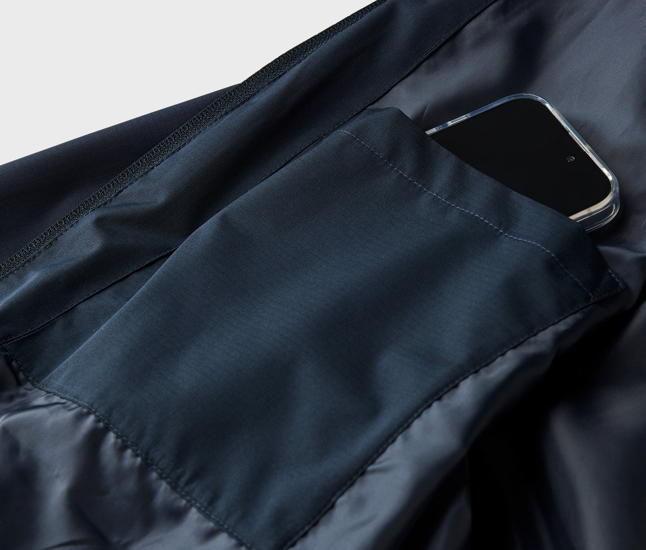 Detailní záběr tmavě modré bundy s chytrým telefonem v kapse.