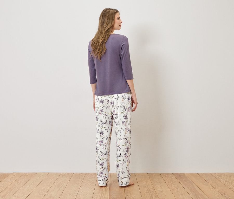 Žena stojí zády ke kameře a má na sobě fialový pyžamový top a bílé pyžamové kalhoty s květinovým vzorem.