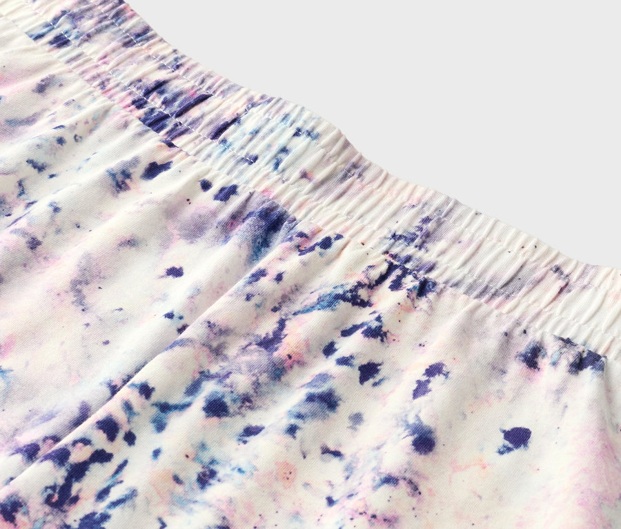 Detailní záběr šortek s elastickým pasem a batikovaným vzorem v fialové, modré a růžové barvě.