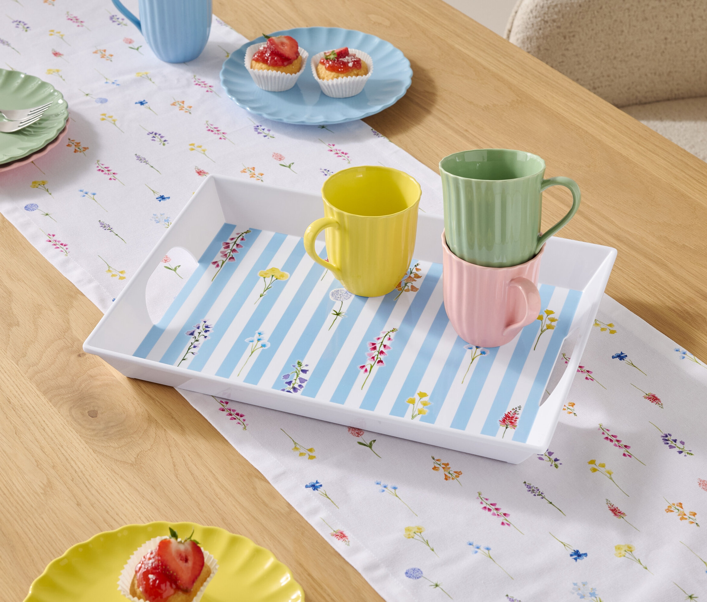 Jídelní stůl s nádobím a šálky na květinovém ubrusu.