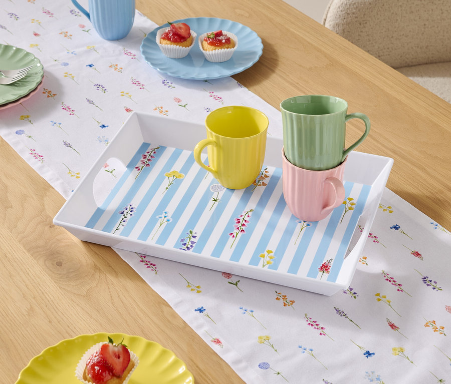 Jídelní stůl s nádobím a šálky na květinovém ubrusu.