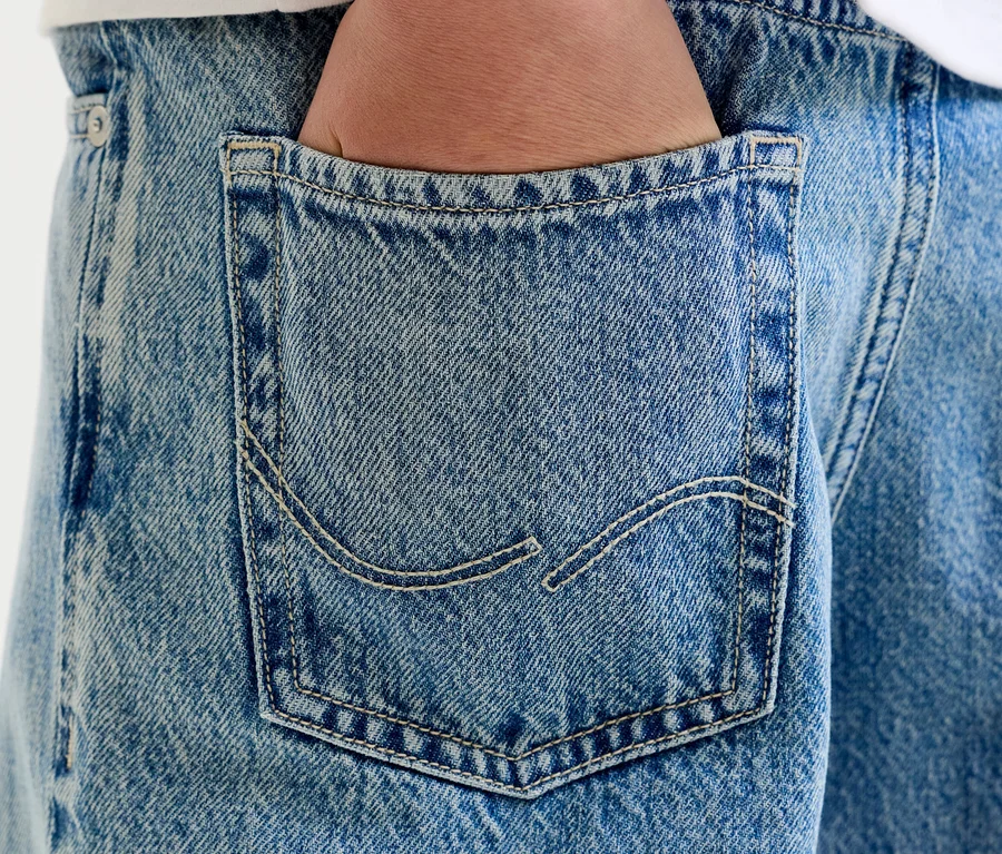 Detail ruky v zadní kapse světle modrých džínů s viditelným prošíváním.
