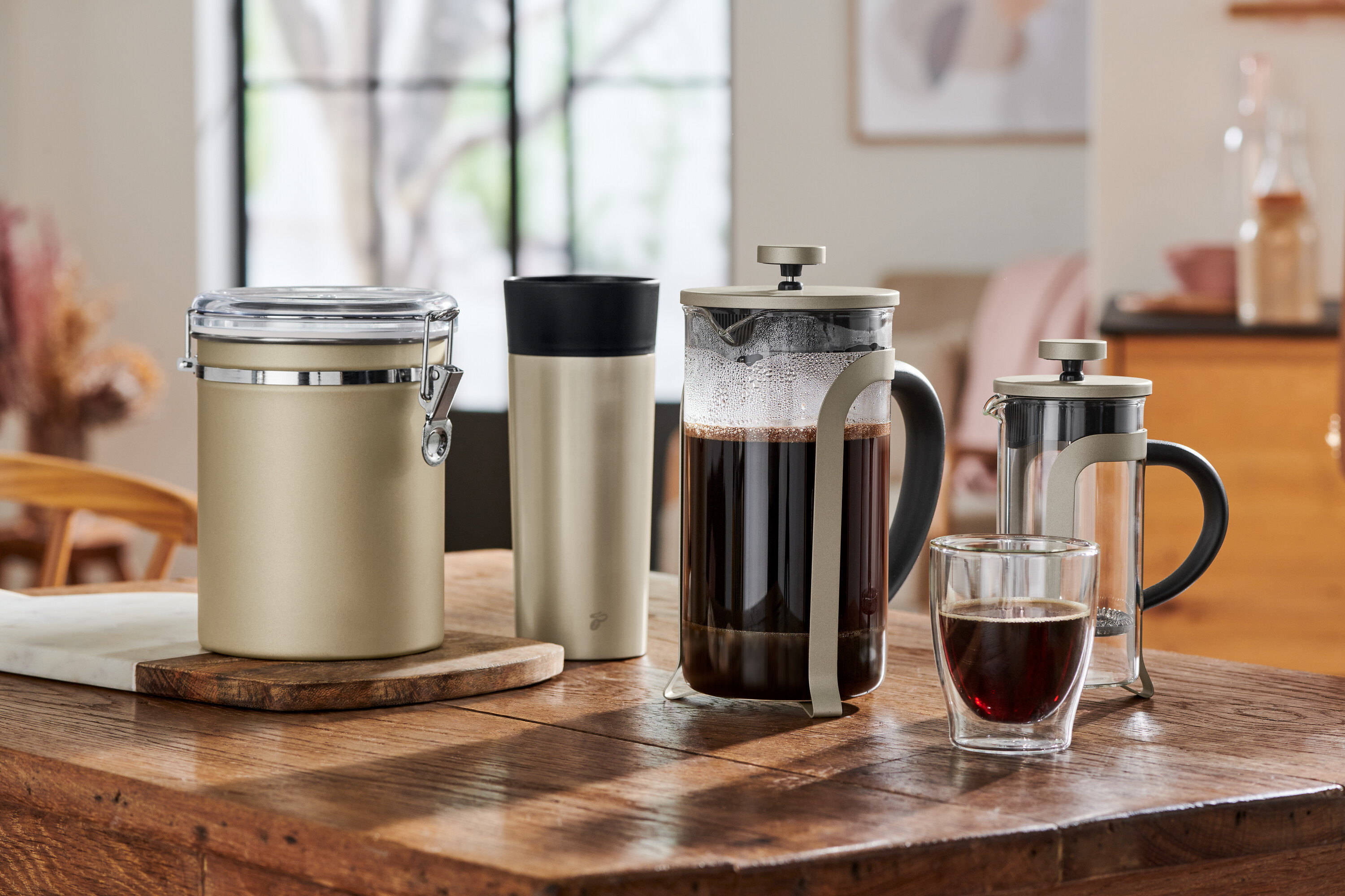 Na dřevěném stole stojí dóza, termoska a french press konvice.