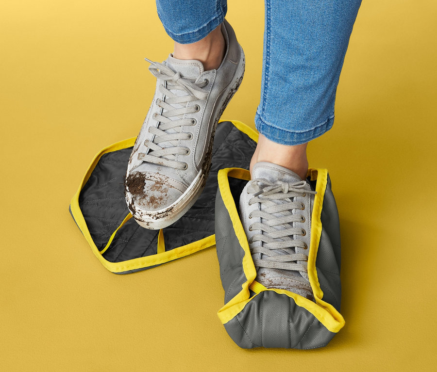 Nohy v džínách. Jedna bota stojí na návleku na boty, druhá má návlek na sobě.