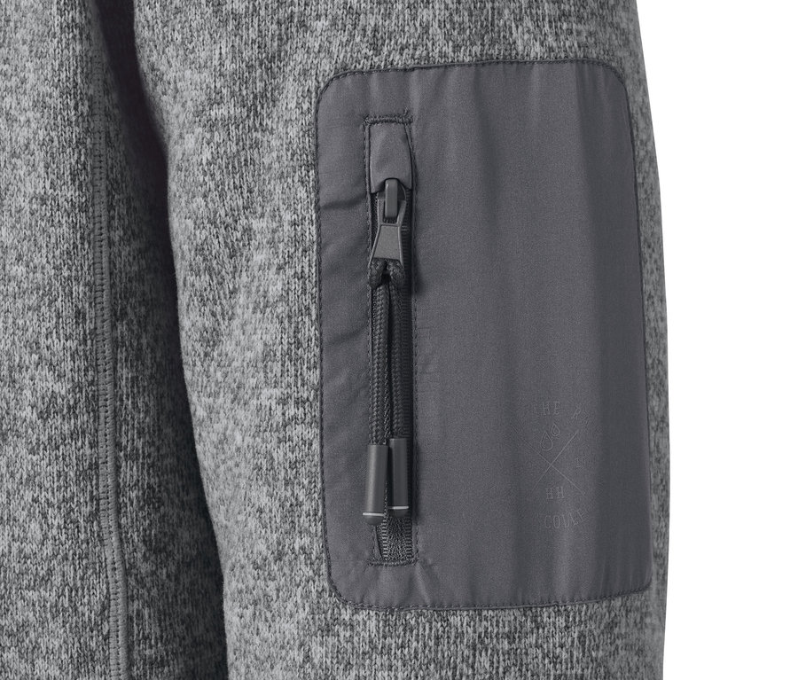 Detail šedé bundy z pleteného fleecu s kapsou na zip.
