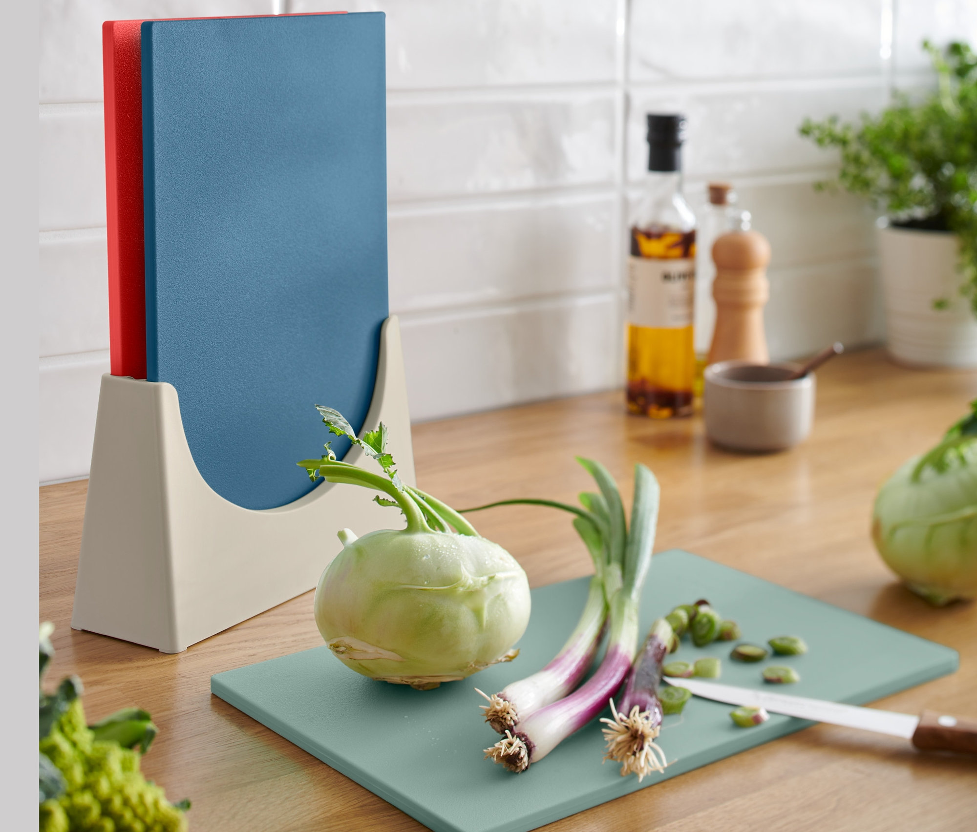 Na kuchyňské lince stojí stojan s krájecími prkénky, 3 ks. Na zeleném prkénku leží nakrájená zelenina.