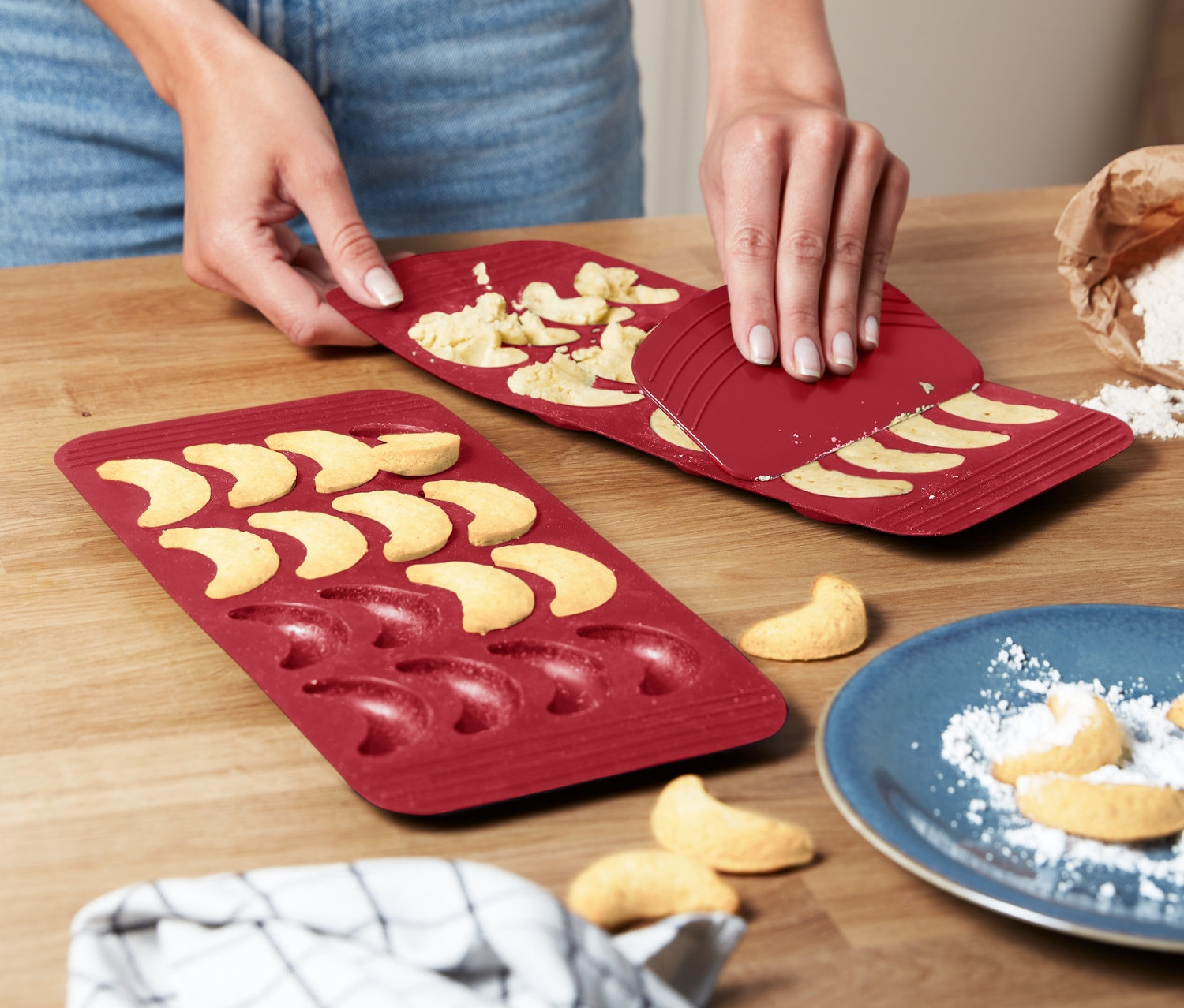 Žena vyklápí vanilkové rohlíčky z 2 ks červených forem na pečení.