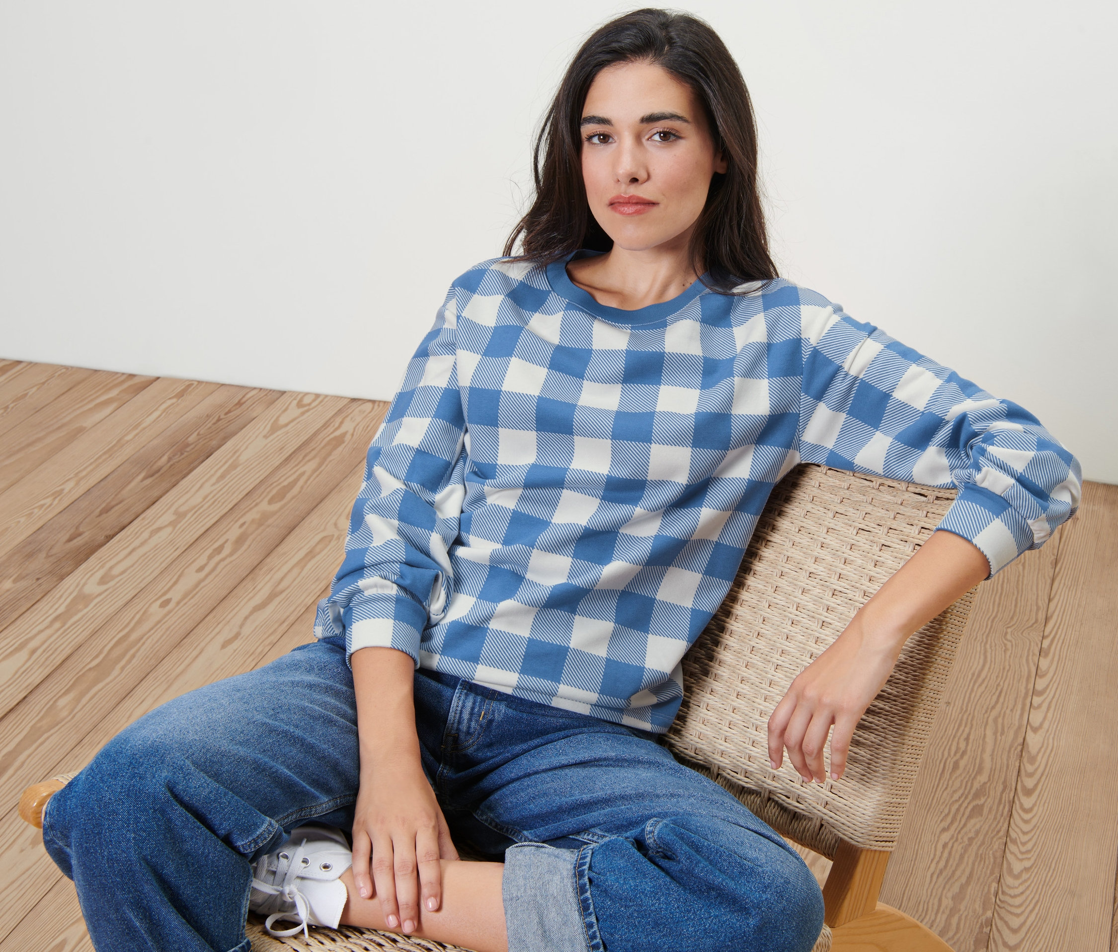 Žena sedí na židli a má na sobě kostkovanou mikinu.