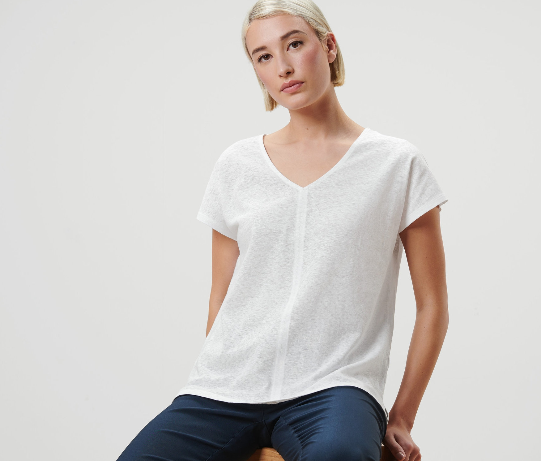 Žena sedí na stoličce a má na sobě krémově bílé lněné tričko.