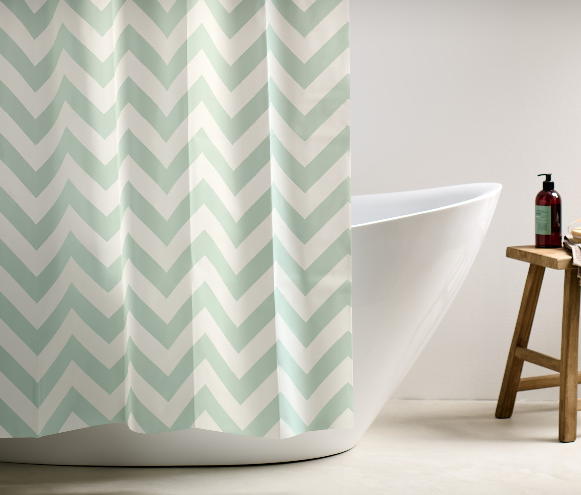 Závěs do sprchy s bílým a světle zeleným cikcakovým vzorem zakrývá část bílé vany.