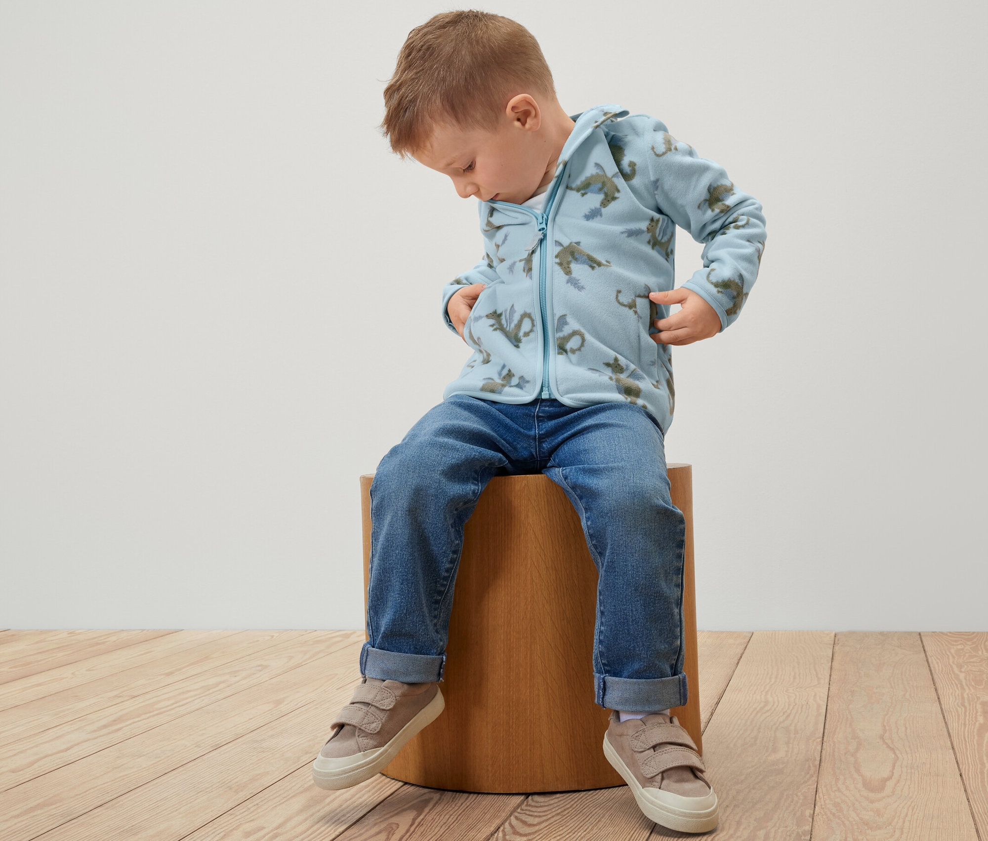 Chlapec sedí na stoličce a má na sobě dětskou fleecovou bundu s motivem dráčka.