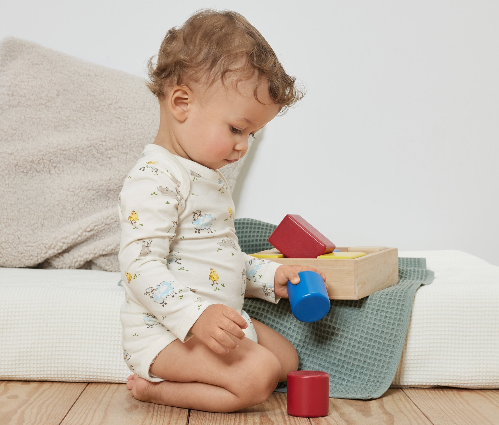 Kudrnaté batole sedí na podlaze a hraje si s barevnými kostkami. Má na sobě modré rostoucí body pro miminka, 3 ks.