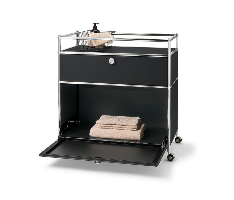 Kovová komoda »CN3« s jednou zásuvkou, výklopnými dvířky a ohrádkou. V horní části je košík s ručníkem a lahvička s pumpičkou. Na spodní polici jsou složené ručníky.