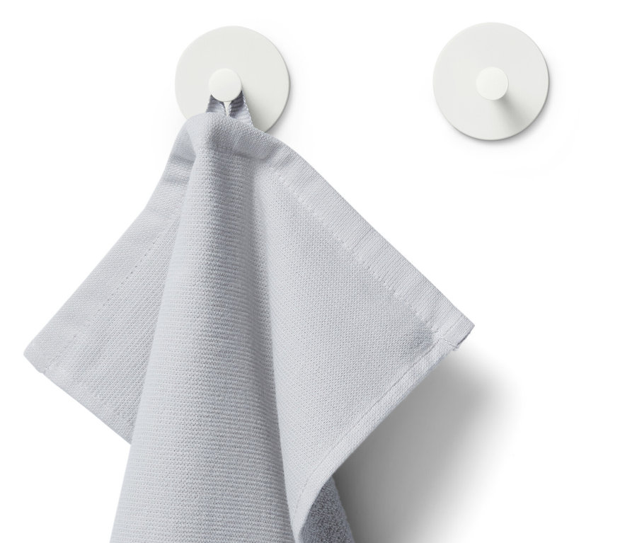 Světle šedý ručník visí na jednom ze dvou bílých háčků.
