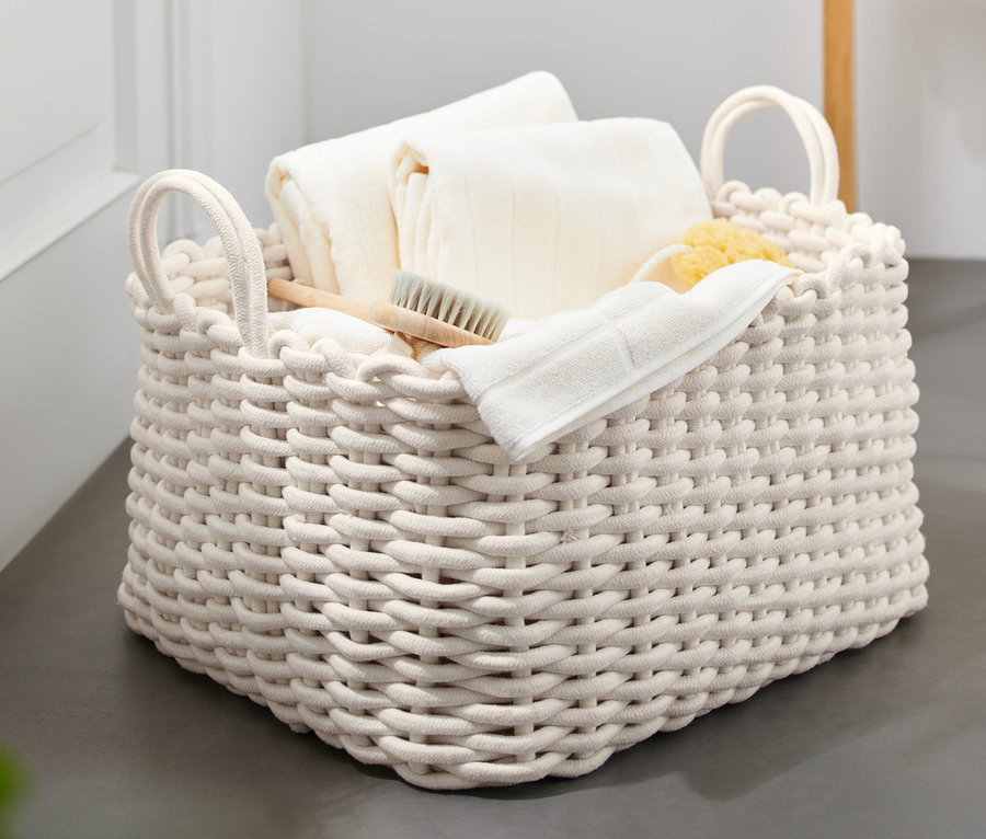 Velký pletený koš se 2 madly plný bílých ručníků, žínky, kartáče a houby.